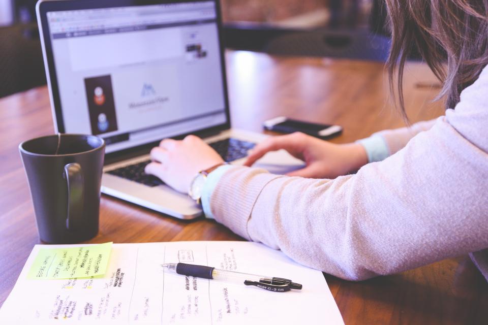 ノートパソコンで作業する人の手元と、机に置かれたメモ書きの用紙とコーヒー